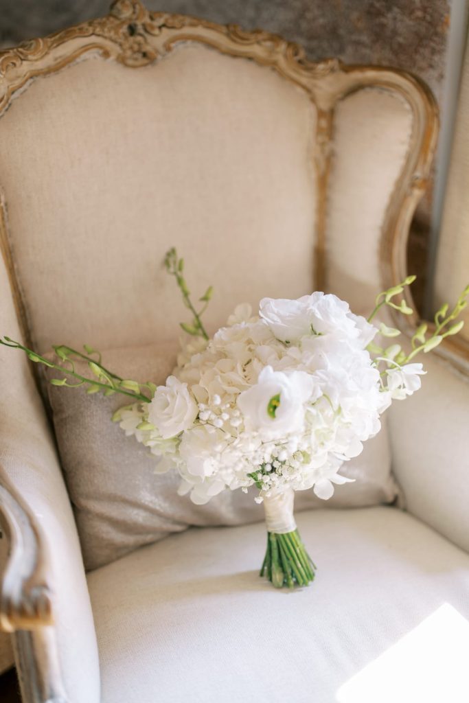 Bouquet de mariage blanc posé sur un fauteuil ancien rembourré.